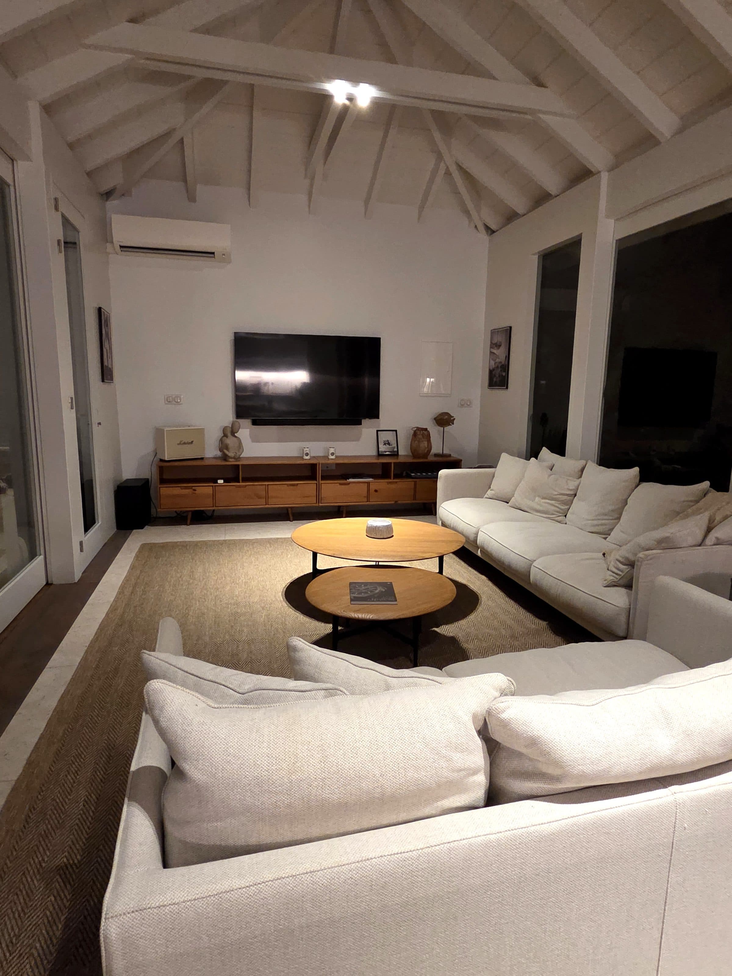 The living pavilion by night: linen sofas around two oak coffee tables under the white timber roof