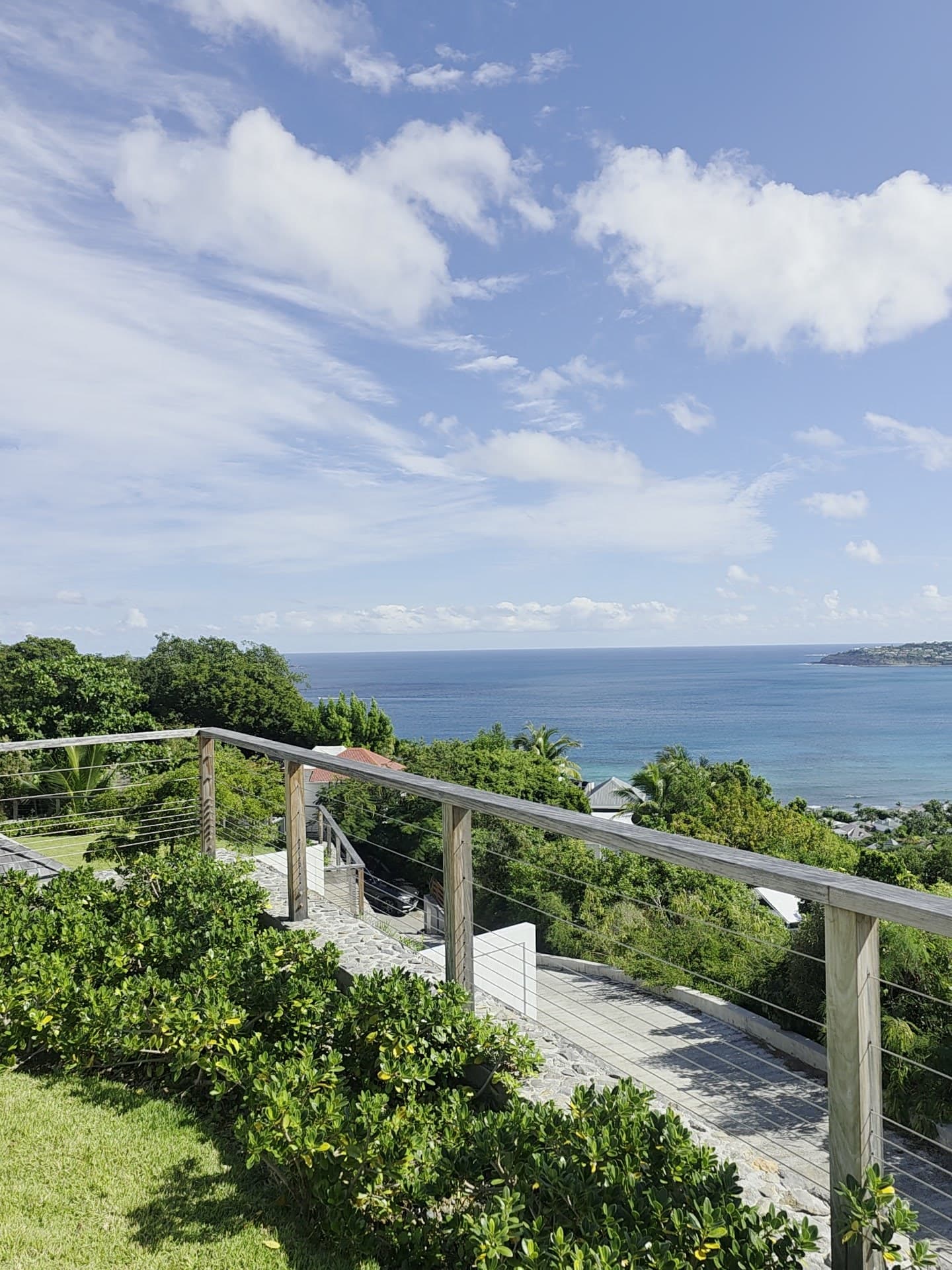 From the upper lawn, the timber and cable railing above the stone steps, with views toward Saint-Jean Bay