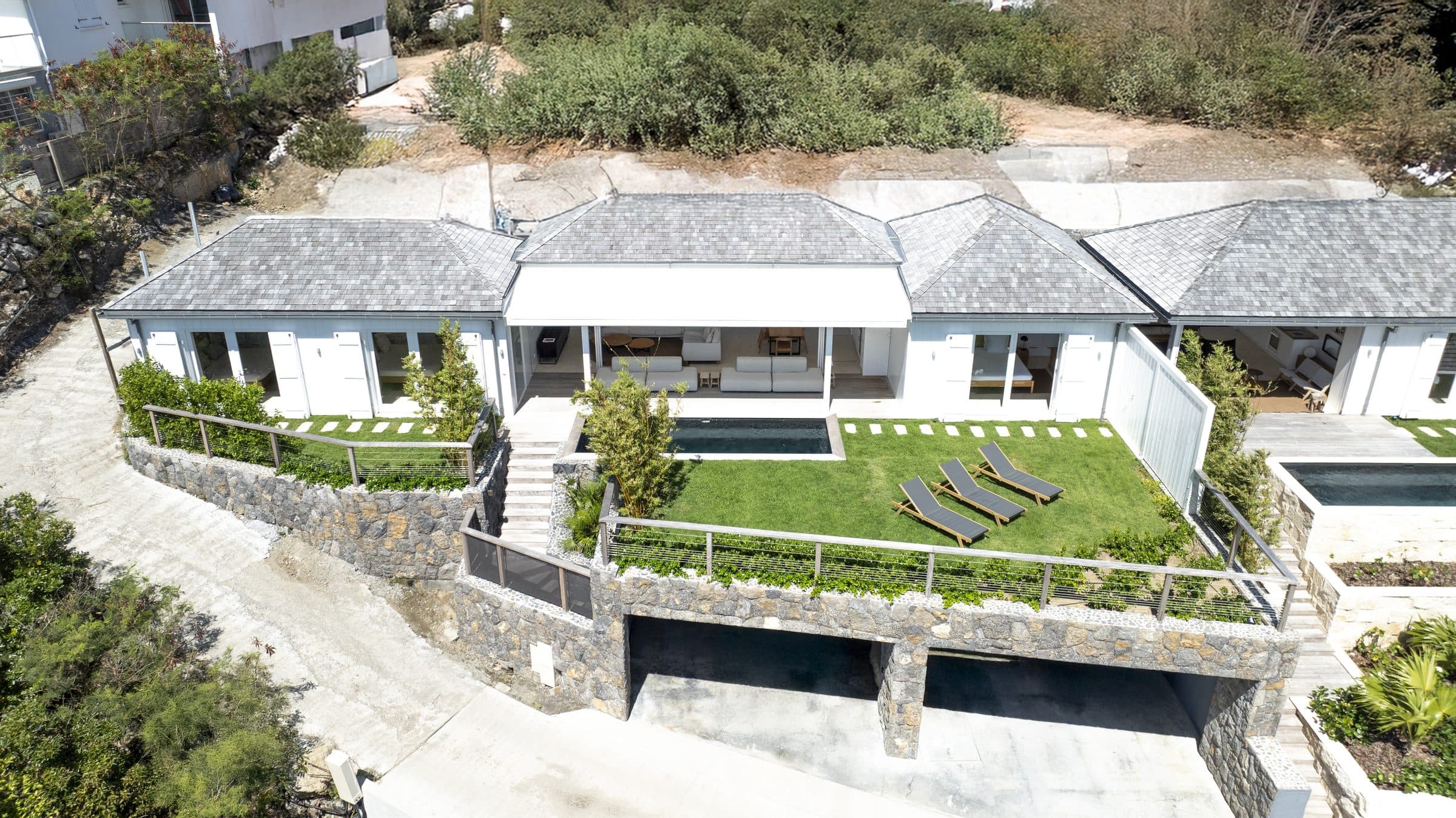 Aerial view of Villa Ciel’s open living pavilion, pool and lawn framed by a stacked-stone retaining wall