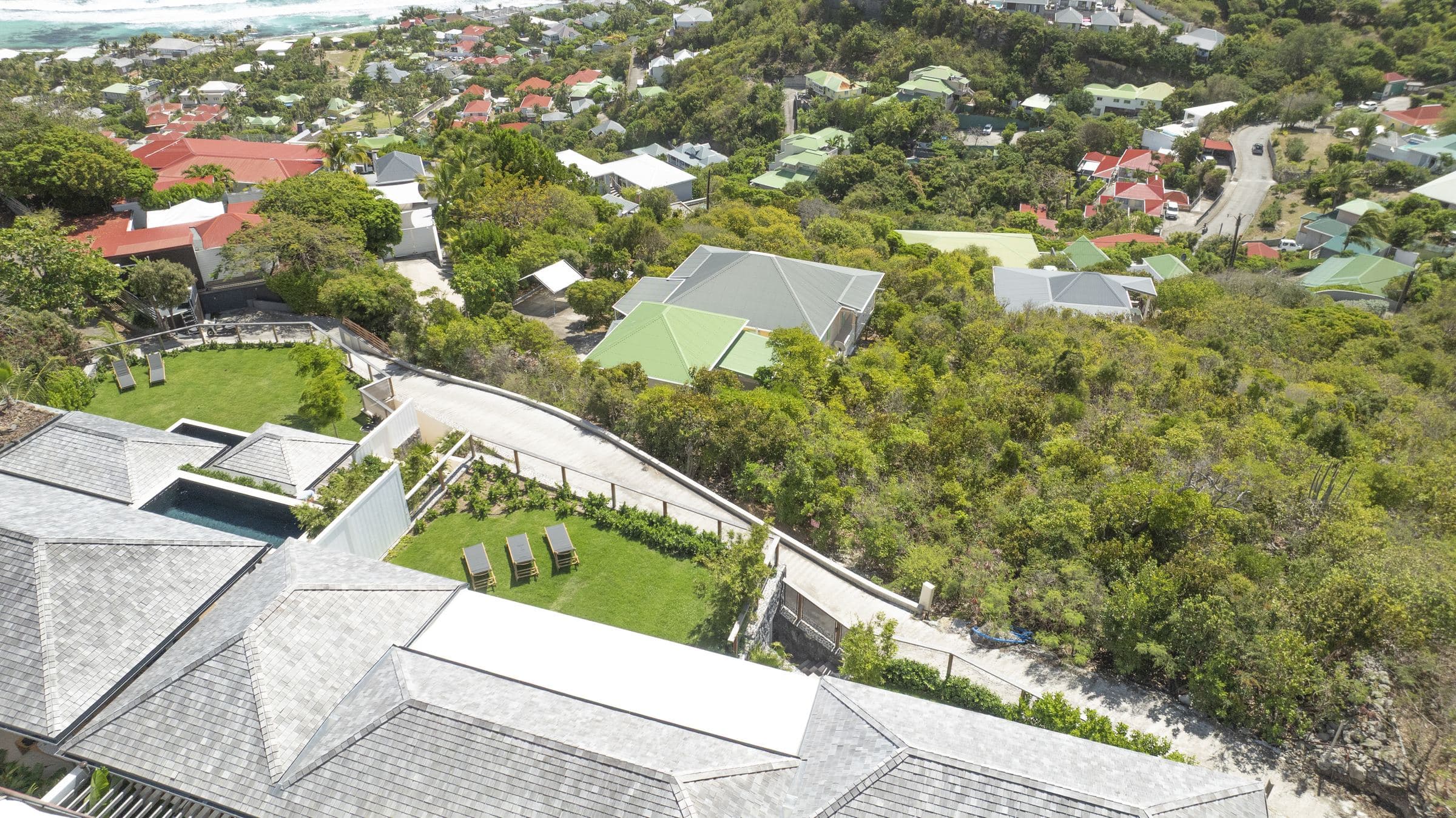 Aerial view across a row of shingled hillside roofs toward the coastline of Saint-Barthélemy