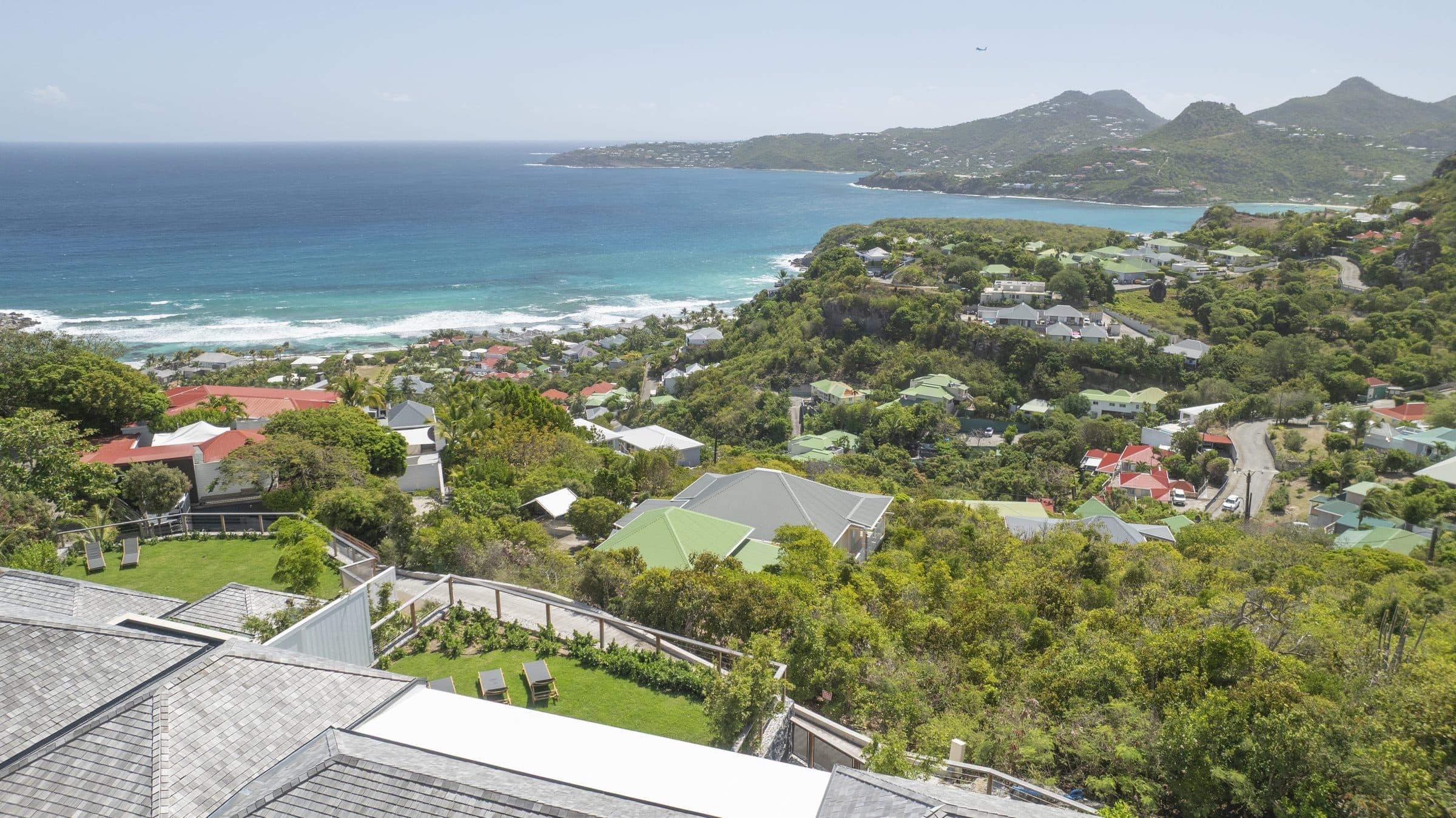 Sweeping aerial panorama of Saint-Jean Bay, turquoise surf breaking at the foot of green hills
