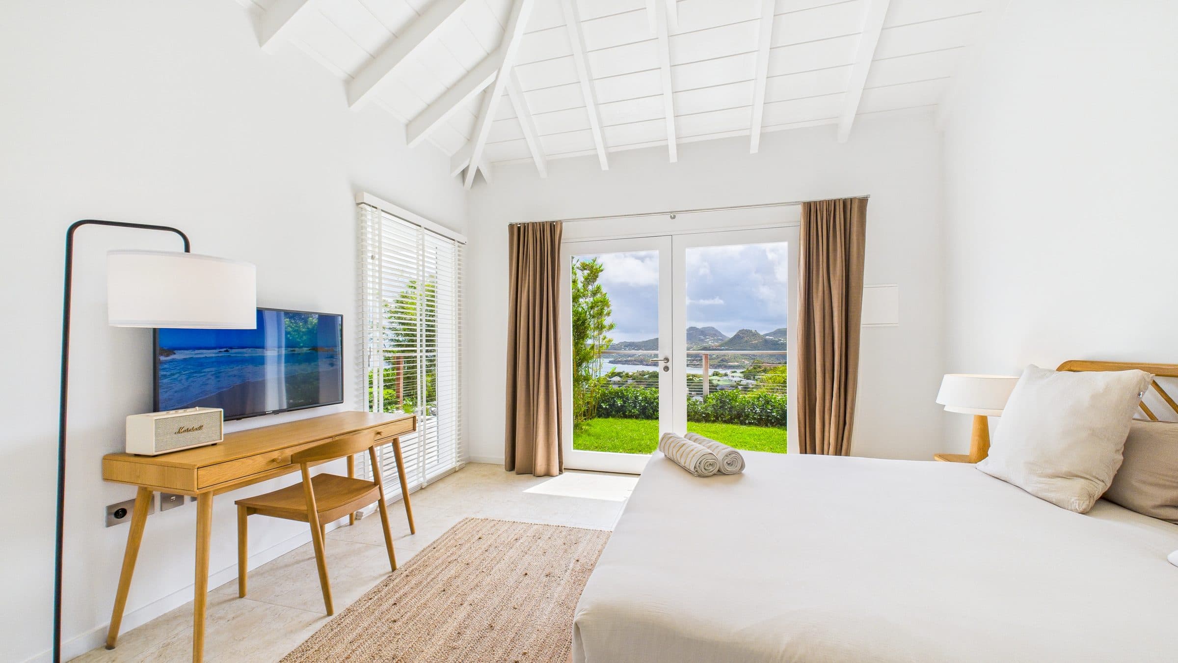 Third bedroom with French doors opening onto the lawn, taupe curtains framing a view of the hills