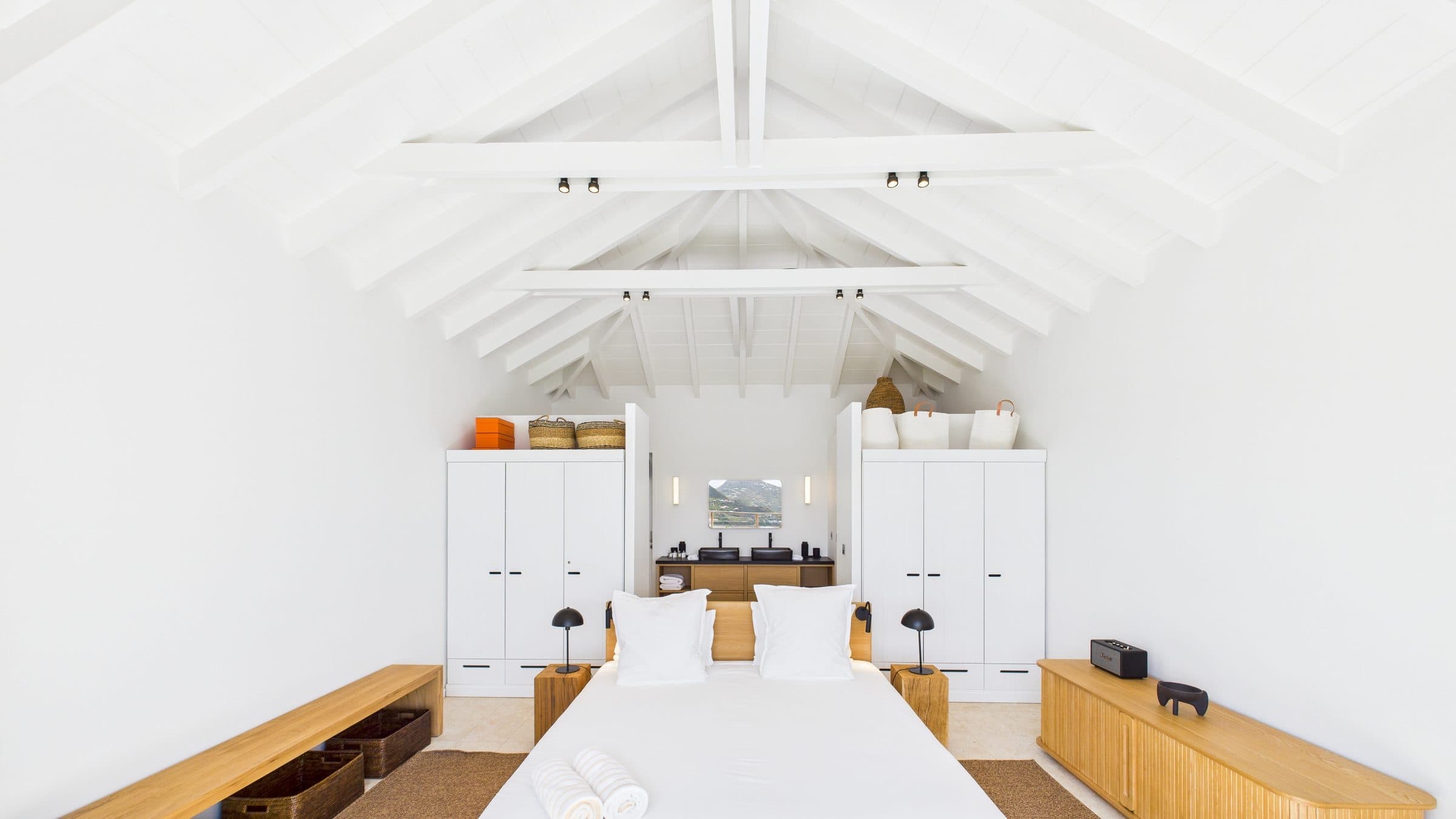 Master bedroom under a soaring white timber-vaulted ceiling, oak bed flanked by twin wardrobes opening onto the ensuite