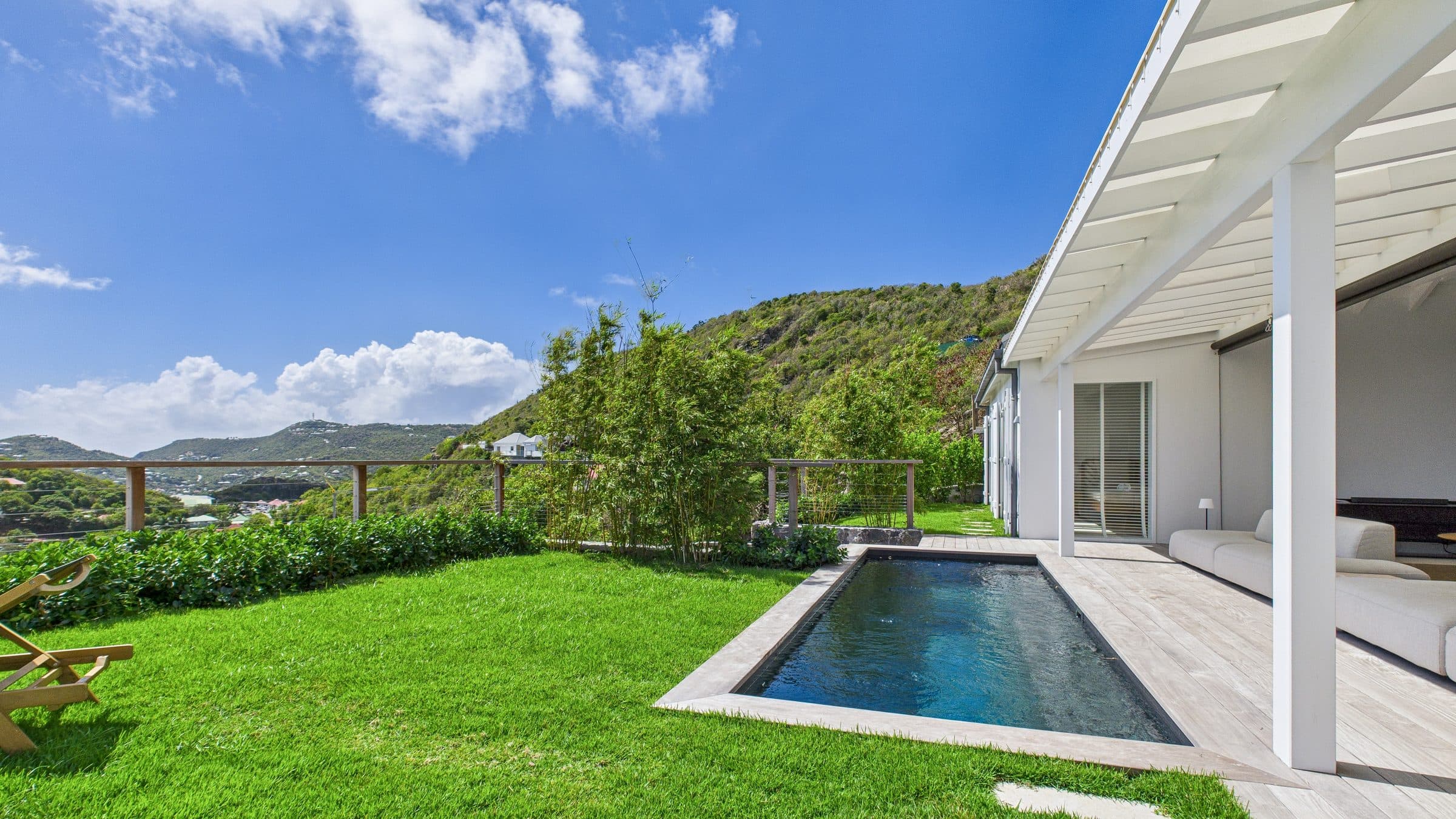 Pool and lawn beside the white pavilion, bamboo hedge screening the view and the green hillside behind
